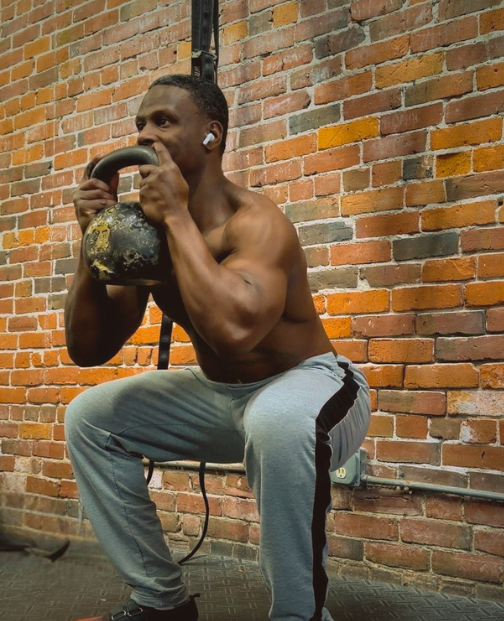 Athlete in a deep kettlebell goblet squat against a brick wall